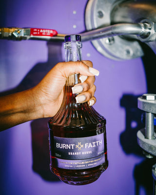 Hand Holding Burnt Faith English brandy bottle